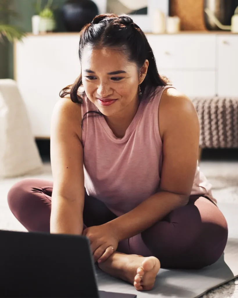 Young woman taking a telehealth appointment while on a yoga mat.